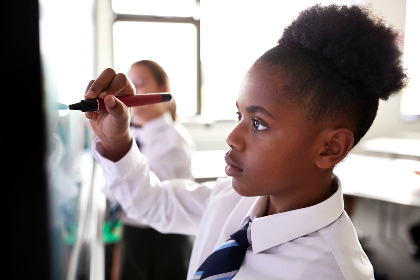A young pupil writing on a whiteboard in a classroom