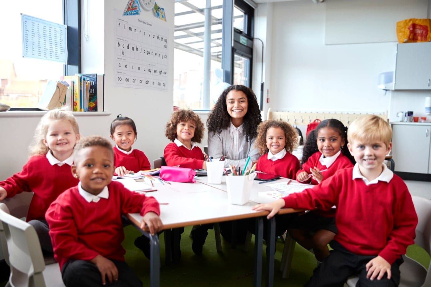 A teacher sitting with a small group of young pupils around a classroom table