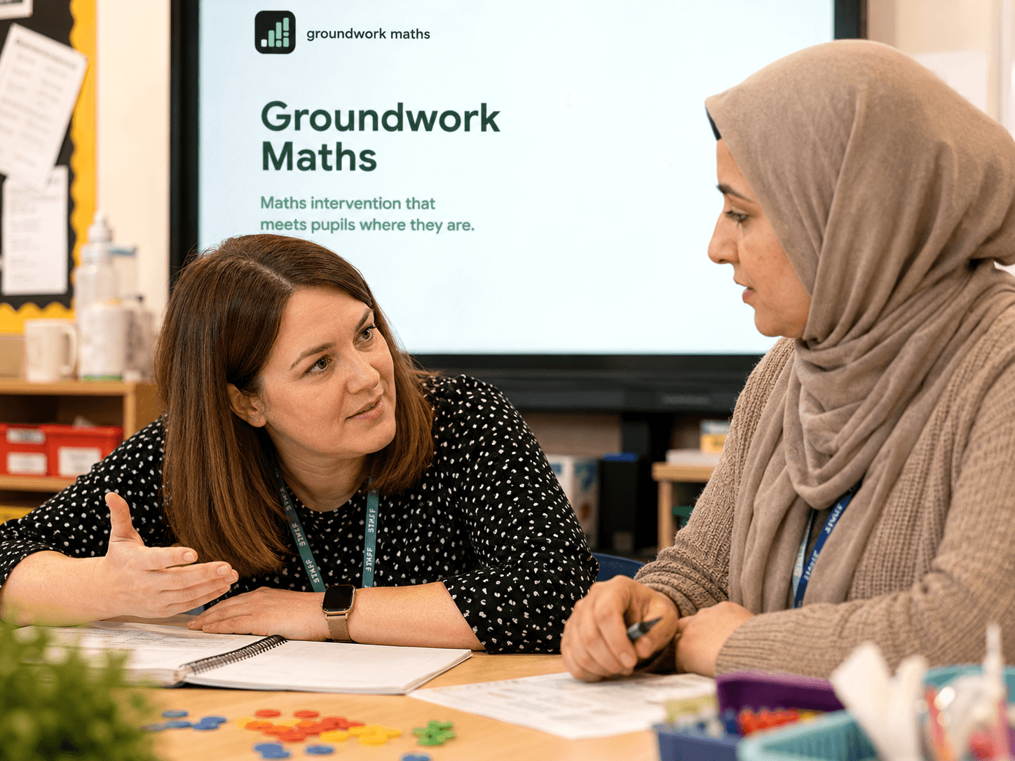 Two teachers discussing Groundwork Maths intervention materials in a classroom.